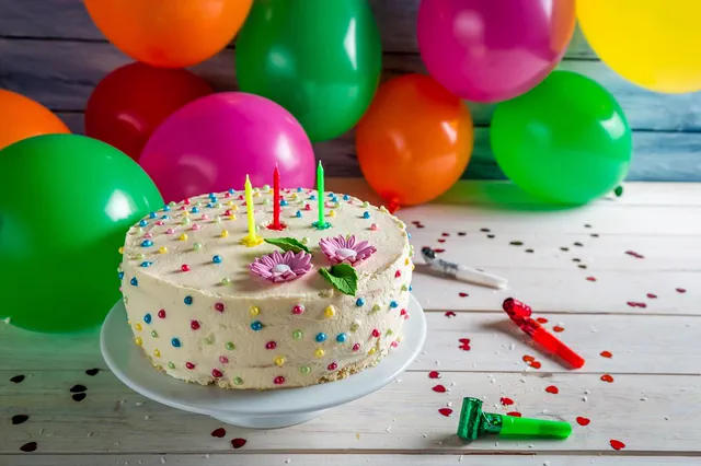 Sprinkle-covered birthday cake with candles and colorful balloons