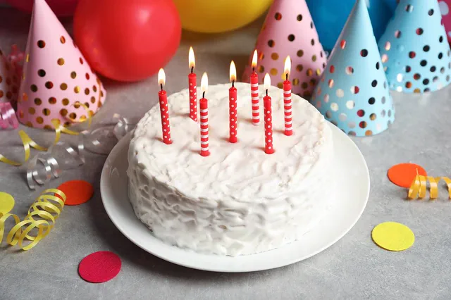 White birthday cake with red candles and party hats