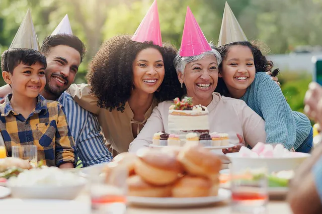 Family in party hats celebrating a grandmother's birthday outdoors