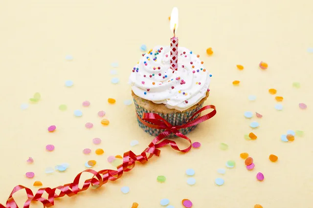 Cupcake with a lit candle, red ribbon and confetti