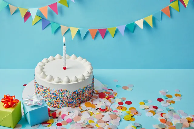 White sprinkle cake with one candle under bunting