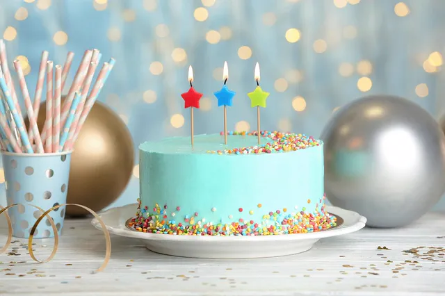 Turquoise sprinkle cake with star candles and silver balloons