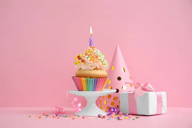 Rainbow cupcake with a candle beside a party hat and gift box