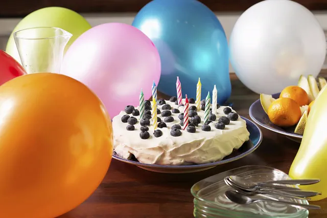 Blueberry birthday cake with candles surrounded by balloons