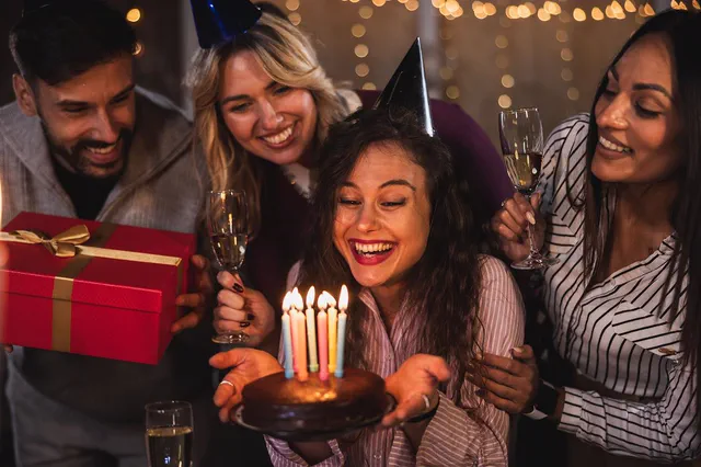 Friends cheering as a woman blows out her birthday candles